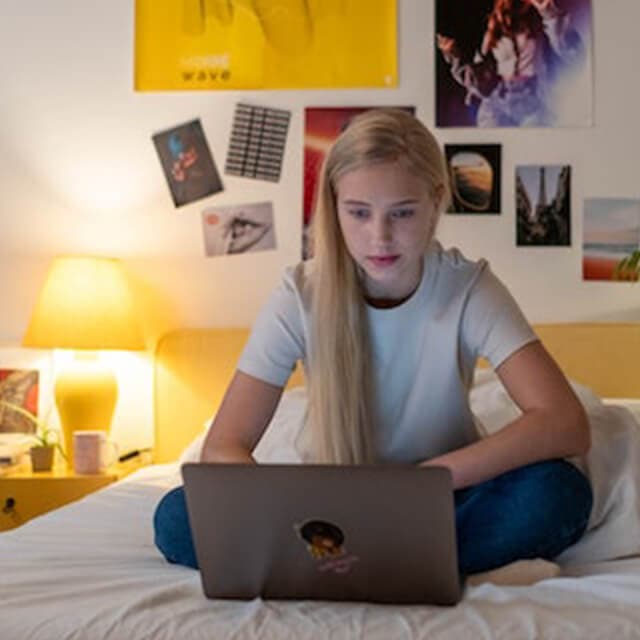 Joven adolescente trabajando con un portátil en su habitación, representando una sesión de asesoramiento filosófico online