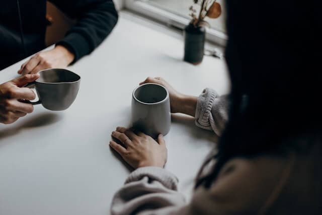 Dos personas conversando frente a frente con tazas de café, evocando una sesión de consultoría filosófica presencial